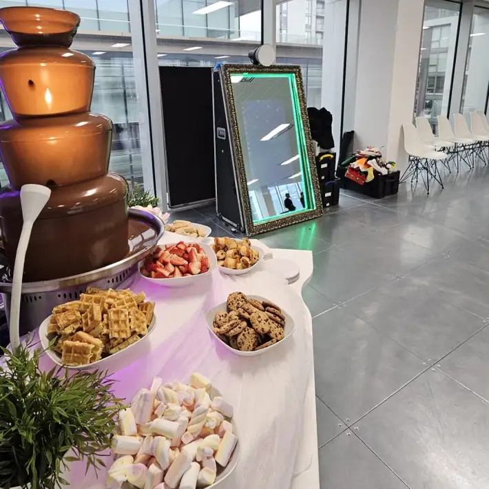 Chocolate fountain with waffles, cookies, and fruit beside a selfie mirror at an office Christmas party for kids in Ireland.