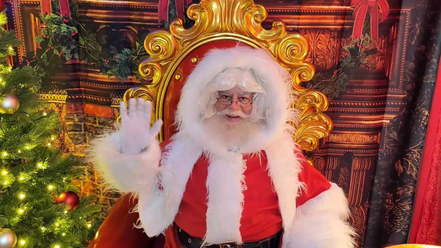 Santa Claus waving from a golden throne beside a Christmas tree at a corporate office kids Christmas party in Dublin, Ireland.