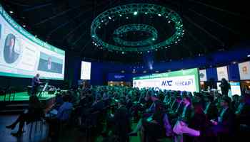 Large audience attending a company kick-off conference in Ireland with keynote speaker on stage, branded screens, and professional event setup by Dynamic Events.