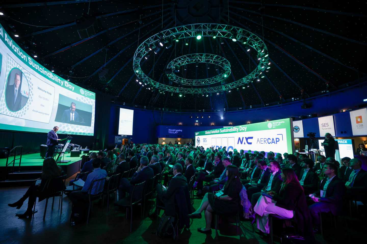 Large audience attending a company kick-off conference in Ireland with keynote speaker on stage, branded screens, and professional event setup by Dynamic Events.